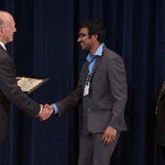 Award recipient in a grey suit smiling and shaking hands with Doctor Potteiger